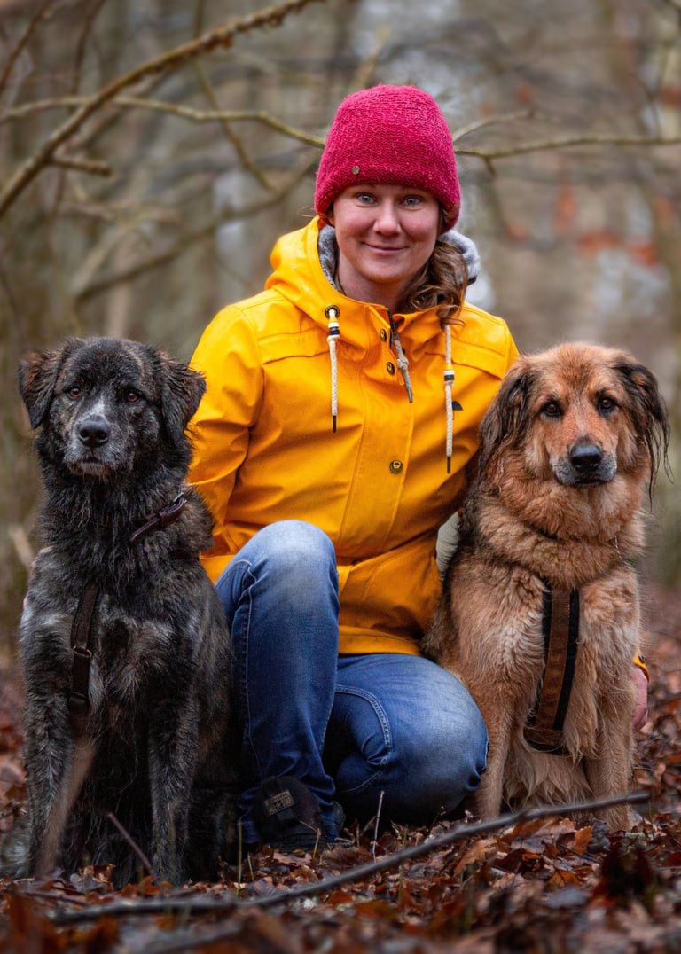 Jo sitzt mit ihren Hunden Rasmus und Emma im Wald